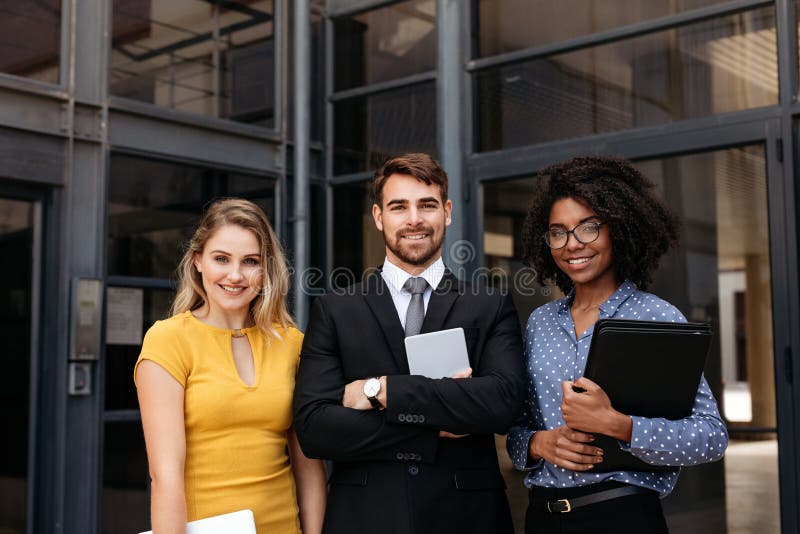 Team of young business professionals standing together in front of office building. Group of multi-ethnic business people in corporate office building. Team of young business professionals standing together in front of office building. Group of multi-ethnic business people in corporate office building